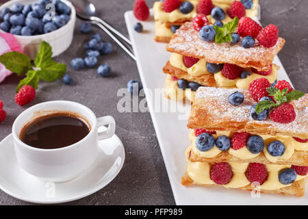 Le français dessert millefeuille de pâte feuilletée et crème pâtissière, framboises, bleuets sur une plaque avec tasse de café et petits fruits sur une table, vue à partir de Banque D'Images