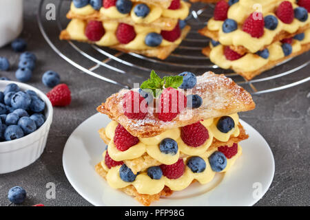 Le français dessert millefeuille de pâte feuilletée et crème pâtissière, framboises, bleuets sur une plaque avec de la crème fraîche et les baies sur une table en béton, vi Banque D'Images