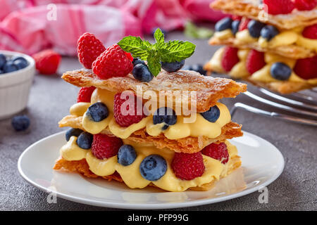 Le français dessert millefeuille de trois morceaux de pâte feuilletée en couches avec crème pâtissière, framboises, bleuets sur une plaque blanche sur une table en béton, Banque D'Images