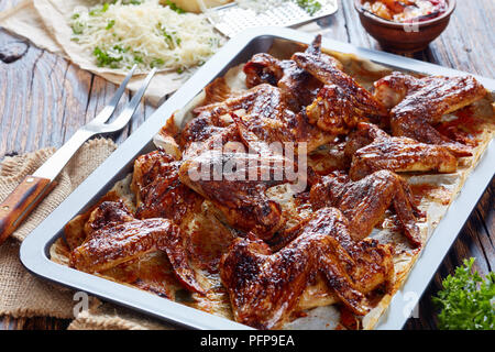 Ailes de poulet croustillant parmesan au four sur une plaque de cuisson sur une vieille table en bois rustique avec salsa aux pêches ingrédients et à l'arrière-plan, l'horizonta Banque D'Images