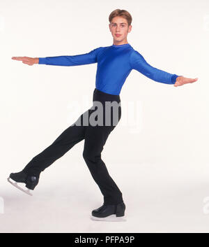 Teenage boy en tenue de patinage sur glace en équilibre sur une jambe, skate, arms outstretched Banque D'Images