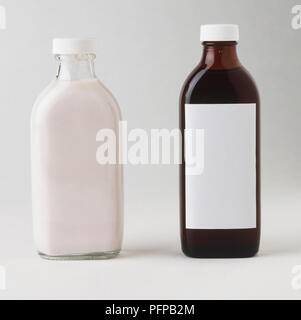Bouteille en verre transparent rempli de crème blanche et un flacon en verre brun avec étiquette vierge rempli de sirop. Banque D'Images