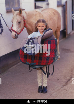 Young Girl standing in front of palomino poney selle après l'untacking maintenant Banque D'Images