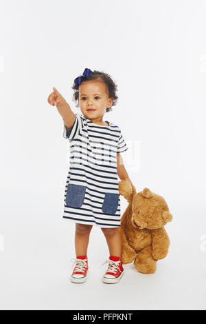 Petite fille en robe stripey jouant avec bear (Modèle âge - 19 mois) Banque D'Images