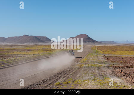 Location de voiture les touristes voyageant sur route poussiéreuse si désert du namib avec collines et fleur jaune et la faune couvrant le sol, bleu clair Ciel d'hiver, Sk Banque D'Images