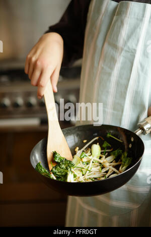 Femme portant un tablier à rayures à l'aide de spatule en bois pour les sautés au wok ingrédients Banque D'Images