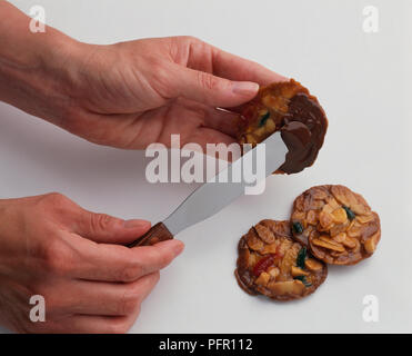 Personne à l'aide de couteau pour répandre le chocolat fondu sur les biscuits florentins, close-up Banque D'Images