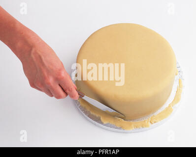 Personne à l'aide de couteau pour enlever l'excès de pâte feuilletée de la base du gâteau, close-up Banque D'Images