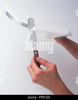 Personne à l'aide de couteau pour enlever l'excès de sugarpaste de gâteau sur gâteau d'argent, close-up Banque D'Images