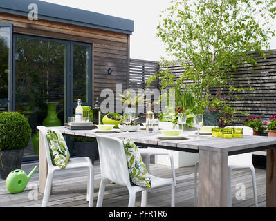 Set de table en bois pour manger et modèle floral coussins sur les chaises en plastique blanc sur le patio en bois, side view Banque D'Images