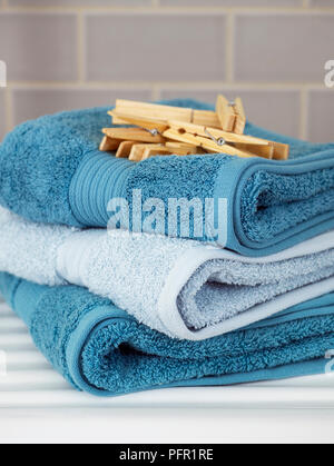 Des pinces à linge en bois sur le dessus de la pile de turquoise et bleu pâle plié serviettes sur étagère dans la salle de lavage, close-up Banque D'Images