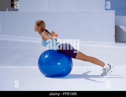Woman lying on fitness ball doing stretching exercice, les bras sur le côté, side view Banque D'Images