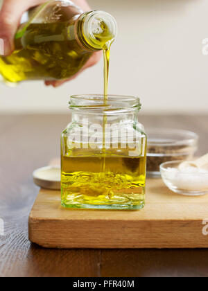 Verser l'huile d'olive dans petit pot contenant du vinaigre de vin blanc (fabrication de vinaigrette) Banque D'Images
