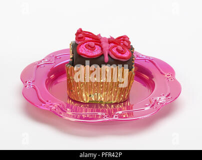Petit gâteau au chocolat avec glaçage papillon rose d'or en cas de gâteau, sur plaque rose Banque D'Images