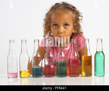 Girl playing 'tuyaux' bouteille, soufflant dans une bouteille qui fait partie d'une rangée de bouteilles remplies de différentes quantités d'eau colorée, 4 ans Banque D'Images