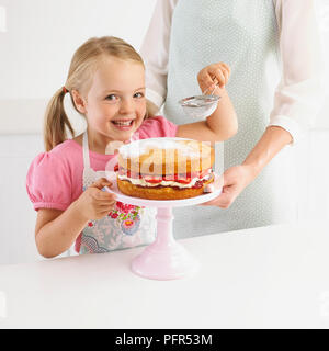 Smiling girl tamisant sucre à glacer gâteau aux fraises, 5 ans Banque D'Images