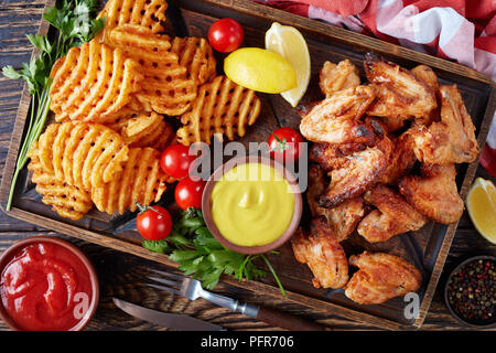 Ailes de poulet frit, Croustillant de pomme de terre frites criss cross sur une plaque d'argile sur une table en bois avec de la moutarde et de la sauce tomate trempage, vue de dessus, à proximité- Banque D'Images