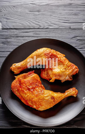 Cuisses de poulet frit avec la peau croustillante d'or sur une plaque noire sur une table en bois, vue verticale de ci-dessus, close-up Banque D'Images