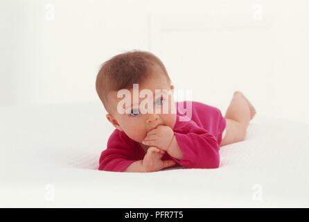 Baby Girl couchée sur son ventre avec ses doigts dans sa bouche Banque D'Images
