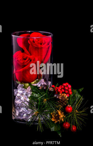 Deux Roses rouges dans un vase avec des billes de verre, de pin, pommes de pin et des petits fruits avec un fond noir Banque D'Images