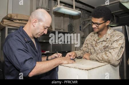 5ème ZONE DES OPÉRATIONS DE LA FLOTTE (28 mai 2018) lance le Cpl. Jerome Johnson, de Columbus, Ohio, et attaché à la 26e unité expéditionnaire de Marines, montre le lieutenant Miguel Estrella, de Killeen, Texas, où à son pochoir correctement dans une combinaison de blanchisserie du navire à bord de la classe Wasp-navire d'assaut amphibie USS Iwo Jima (DG 7), le 28 mai 2018. Iwo Jima, homeported à Mayport, en Floride, est le déploiement de la 5e flotte américaine zone d'opérations à l'appui d'opérations de sécurité maritime de rassurer les alliés et partenaires, et de préserver la liberté de navigation et la libre circulation du commerce dans la région. Banque D'Images