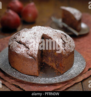 Gâteau au chocolat et poire sur plaque gris saupoudrés de sucre glace dont la tranche sur la plaque en arrière-plan, close-up Banque D'Images