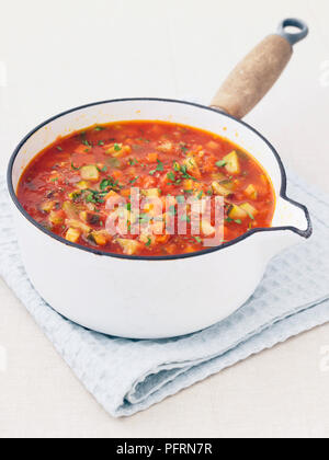 Soupe aux légumes épais avec le céleri, les carottes, les courgettes et les morceaux de tomate, garnie de persil haché dans une casserole, blanc sur un linge plié Banque D'Images