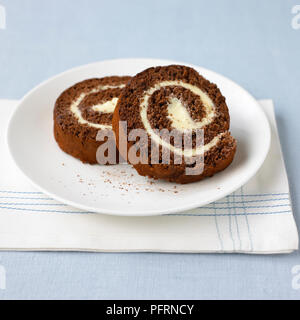 Buttercream chocolat et tranches de rouleau Suisse servi sur assiette blanche sur une serviette pliée et nappe bleue Banque D'Images