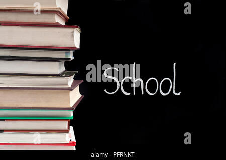 Le mot "école" écrit à la craie sur un tableau noir, à côté d'une pile de livres Banque D'Images