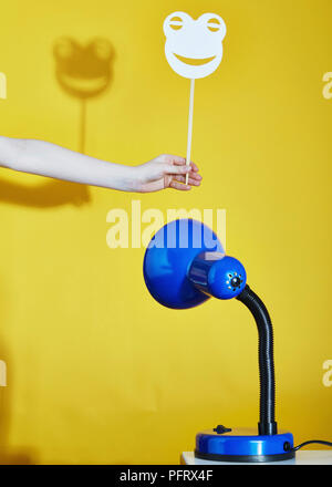 Lampe de table bleu jette une ombre d'un masque de grenouille sur un fond jaune Banque D'Images