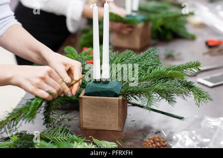 Une femme décore un arrangement de Noël avec des bougies. Mains de près. Master class sur l'apport d'ornements décoratifs. Décoration de Noël avec leurs propres mains. La fête du nouvel an. Flower shop Banque D'Images