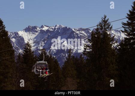 Garmisch-Partenkirchen, Allemagne - 7 avril 2018 - cabine d'un ascenseur de ski avec des skieurs ; forêts et de magnifiques couverts de neige Alpes en arrière-plan Banque D'Images