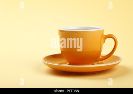 Près d'un jaune pleine tasse de thé ou de café sur une soucoupe sur fond de papier pastel, low angle view Banque D'Images