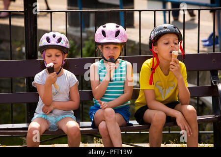 UK, Cornwall, Padstow, le Strand, de jeunes enfants portant des casques de bicyclette de manger des glaces en soleil Banque D'Images