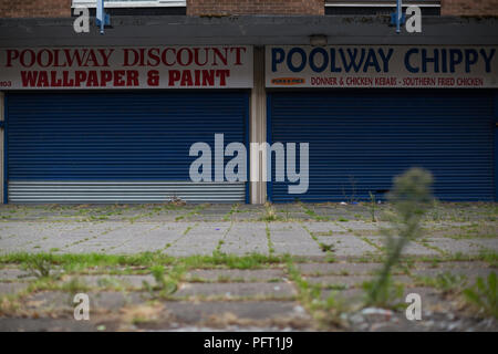 Les mauvaises herbes pousser devant ses volets aux boutiques du centre commercial à l'abandon en Poolway Garretts Green, Birmingham. Construit en 1961, il fut une prospère centre de vente au détail avec les collectivités locales et grands magasins de marque, mais est devenue une ville fantôme, quelques mois après la clôture. Banque D'Images