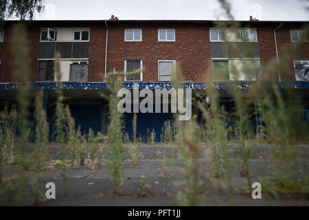 Les mauvaises herbes pousser devant ses volets aux boutiques et appartements au centre commercial à l'abandon en Poolway Garretts Green, Birmingham. Construit en 1961, il fut une prospère centre de vente au détail avec les collectivités locales et grands magasins de marque, mais est devenue une ville fantôme, quelques mois après la clôture. Banque D'Images