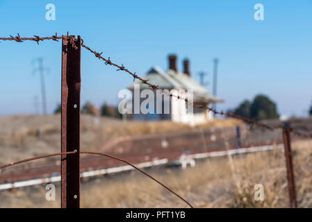 Une vieille clôture de barbelés rouillés avec les lignes de chemin de fer et d'une vieille station de chemin de fer ou à l'arrière-plan flou Banque D'Images