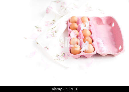 Boîte rose avec des oeufs de poule. PEARA et une serviette avec des fleurs pour la décoration. Oeufs sur un fond blanc. Pour Pâques. Vue d'en haut Banque D'Images