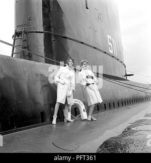 La mode des années 1960. Deux modèles de mode en photo à bord du sous-marin britannique Orpheus. Le sous-marin est ancrée dans le port de Stockholm. Les modèles portent les automnes de la mode d'imperméables. La Suède Mai 1962 Banque D'Images