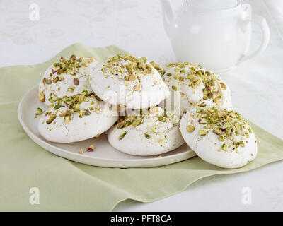 Grande Assiette de meringues pistaches sur une serviette vert pâle avec théière blanche en arrière-plan Banque D'Images