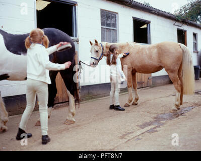 Deux jeunes filles dans leurs poneys de toilettage avant d'équitation de cour stable Banque D'Images