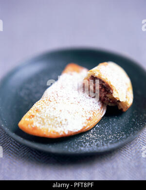 Ravioli di Carnalivari (ravioli de l'Italie du Sud) sur une plaque noire, une pièce à moitié mangé, saupoudrés de sucre glace Banque D'Images