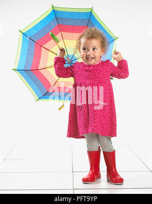 Petite fille (2 ans) portant des bottes wellington et holding umbrella Banque D'Images