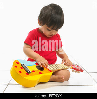 Bébé garçon (16 mois) assis tenant la guitare enfants colorés Banque D'Images