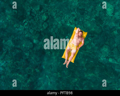 Homme sur matelas gonflable jaune clair avec l'eau de mer en fond rocheux. concept de vacances d'été Banque D'Images