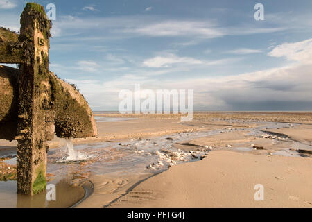 Tuyau d'évacuation d'eau des terres avec l'écoulement à travers un canal coupe une plage de sable fin ; plus de pluie a promis à l'horizon. Banque D'Images