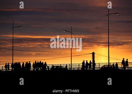 Silhouettes de personnes et de voitures traversant le pont au coucher du soleil, des couleurs éclatantes, scène urbaine Banque D'Images