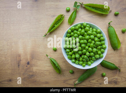 Un plein bol de petits pois frais, jardin biologique qui ont été fraîchement cueilli et retirés de leurs gousses sur une table en bois rustique. Banque D'Images