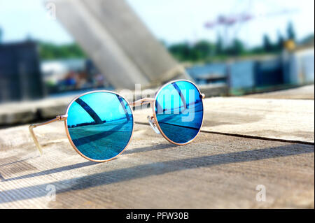 Miroir à la mode lunettes avec verres bleus sur le soleil se coucher sur un sol en bois reste voyage reflète dans verres Banque D'Images