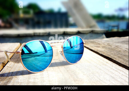 Miroir à la mode lunettes avec verres bleus sur le soleil se coucher sur un sol en bois reste voyage reflète dans verres Banque D'Images